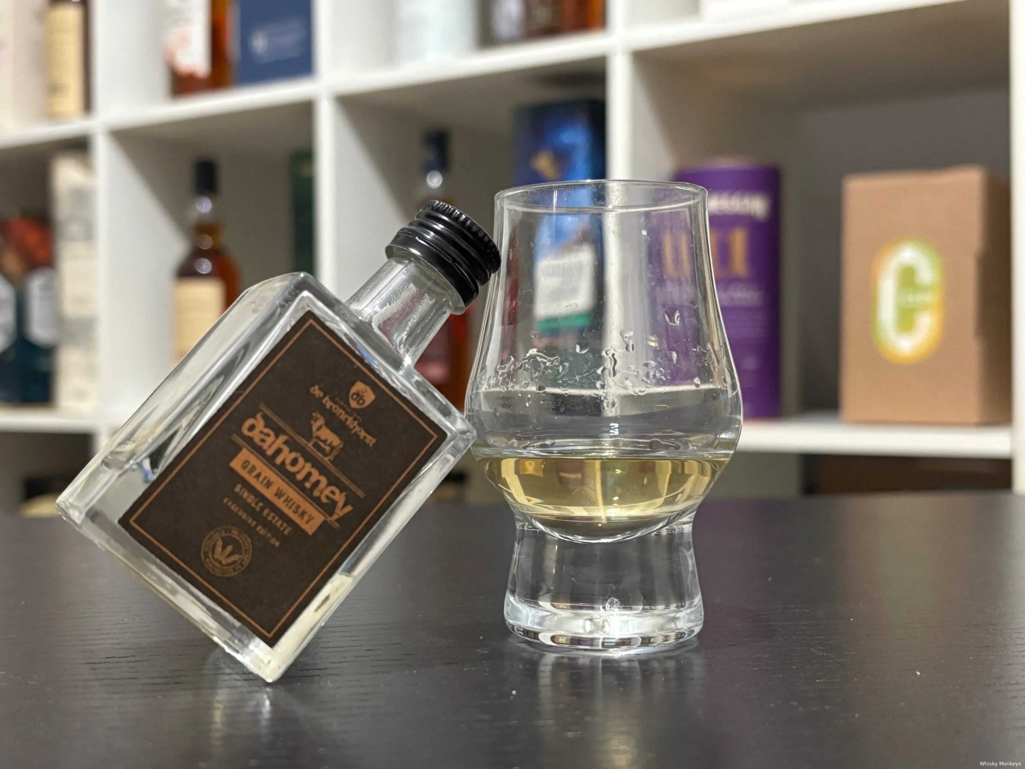 dahomey peated grain fles op een tafel met een glas whisky waar de fles tegenaan leunt