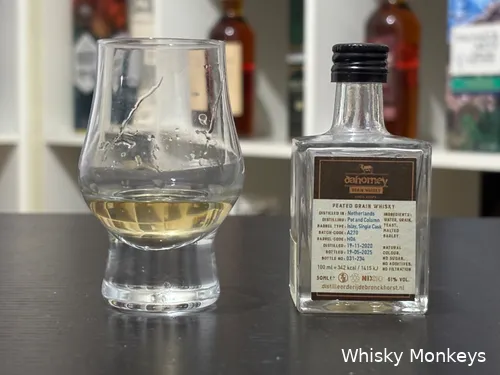 dahomey peated grain bottle on a table with a glass of whisky in front of a cupboard. The specifications of the grain whisky are visible.