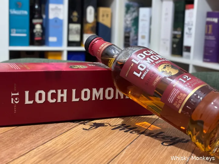 The bottle of Loch Lomond 12 YO on the box and in front of a whisky cabinet