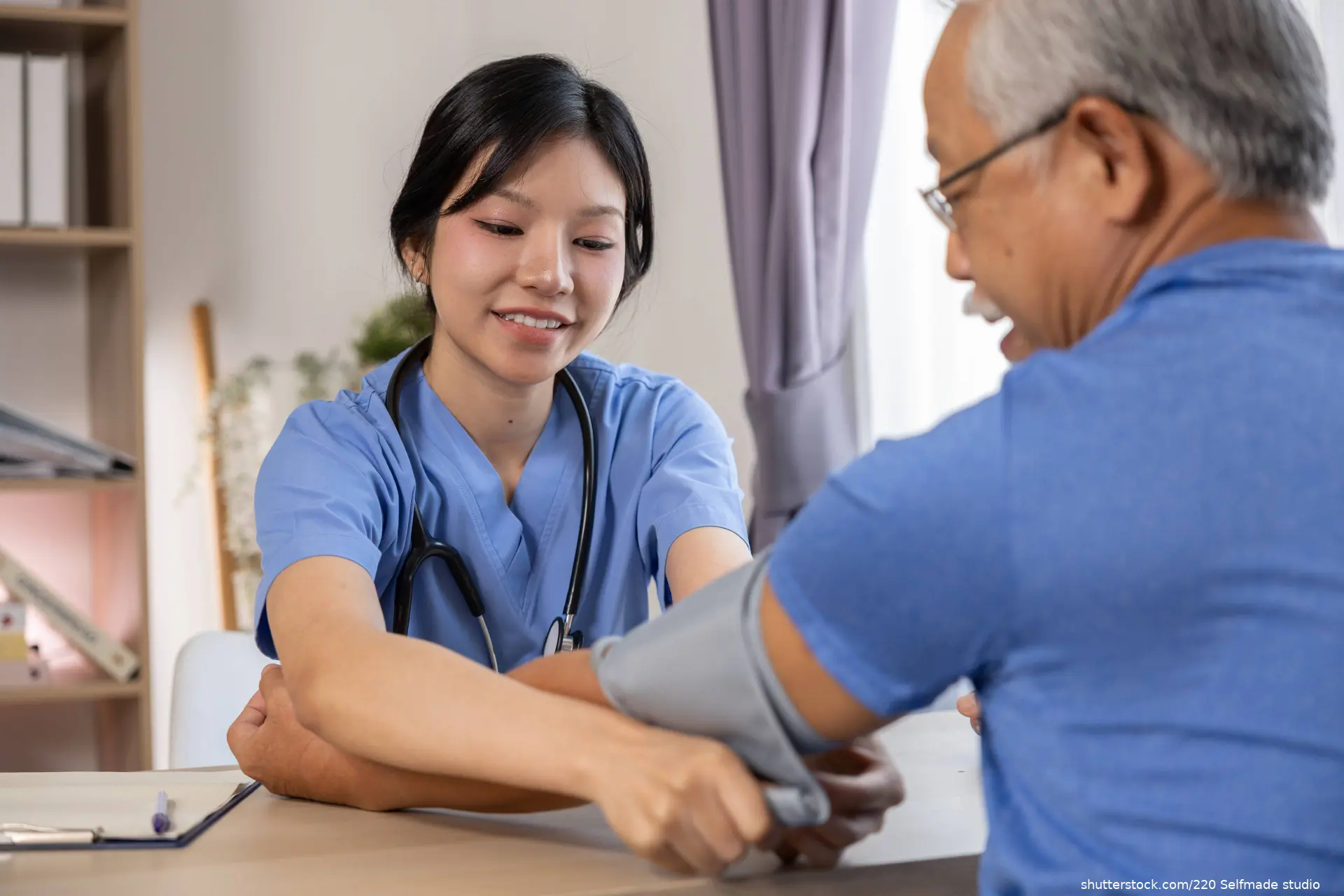Happy young female nurse measuring blood pressure of smiling senior citizen