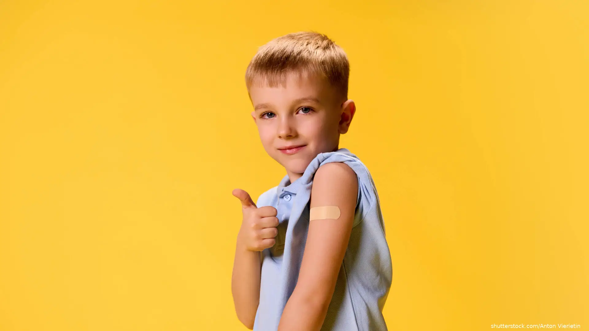 young boy with bandaid on arm giving thumbs up