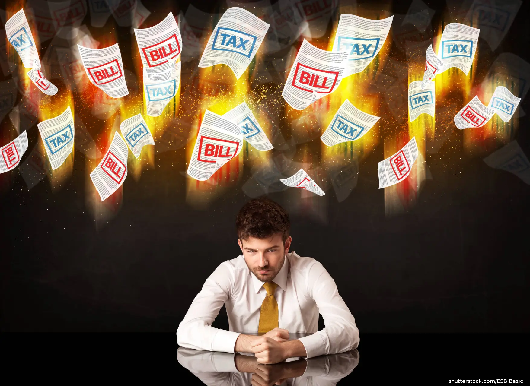 man sitting at desk with tpapers flying overhead showing taxes and bills due