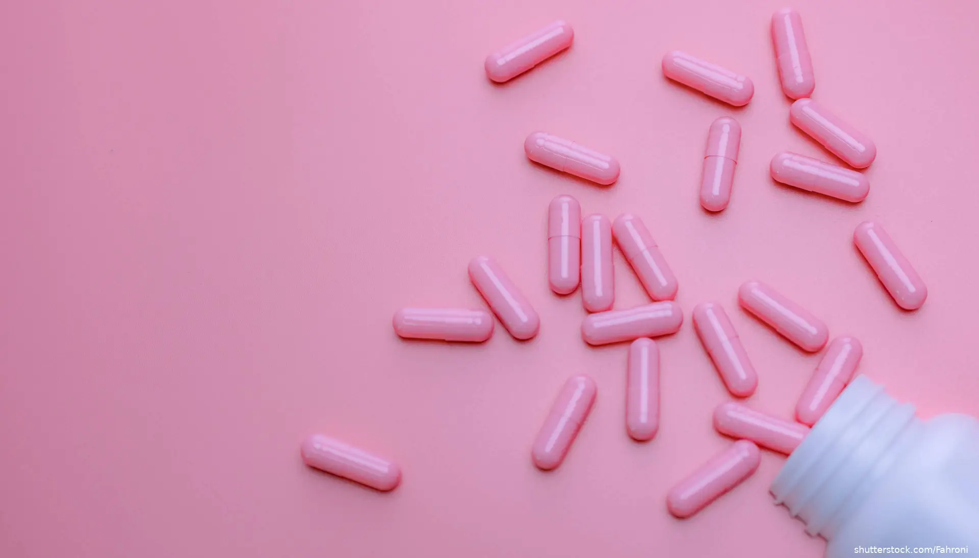 Pink capsules pouring out of bottle onto pink background
