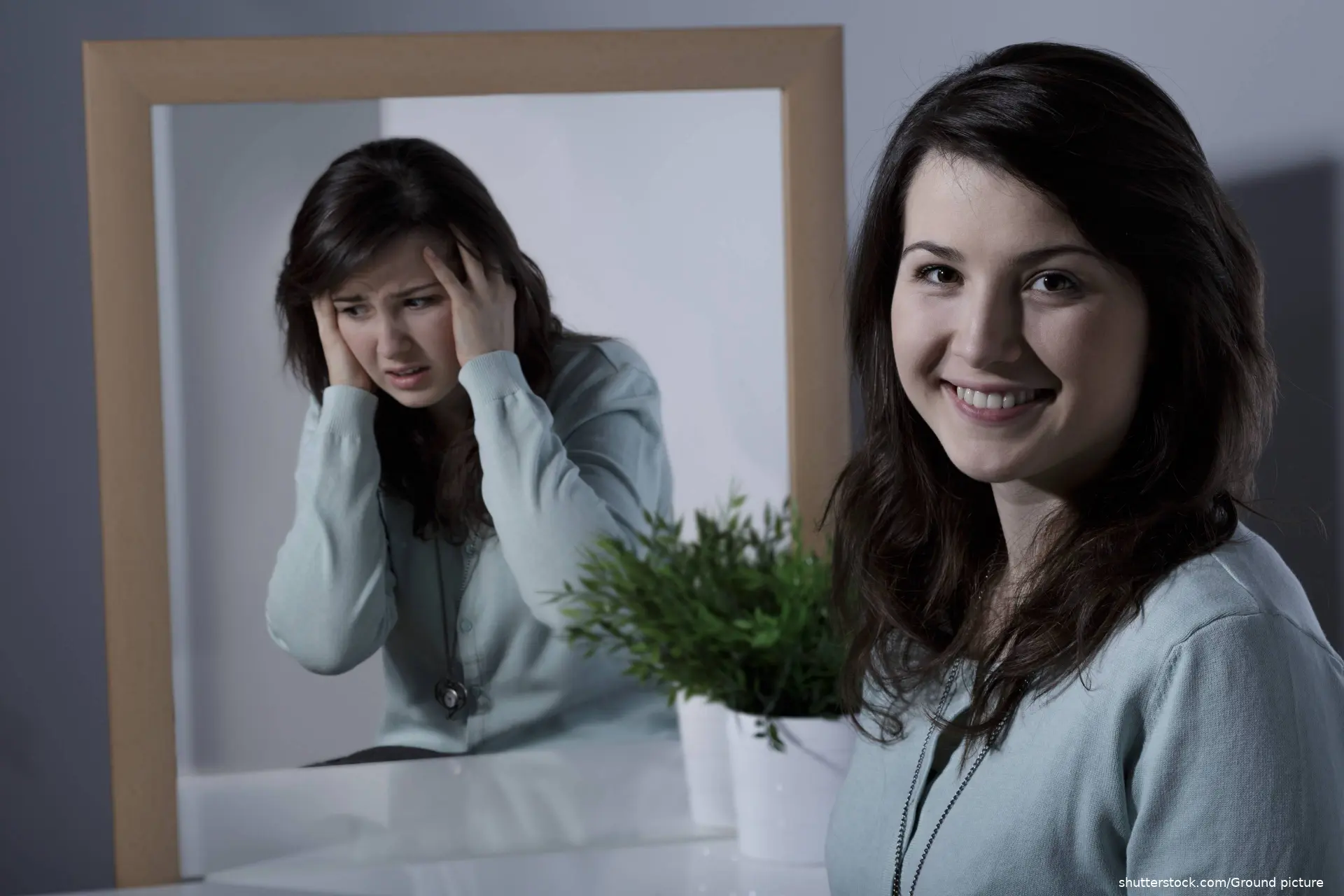 Smiling pretty young girl with bipolar disorder and her troubled reflection in mirror