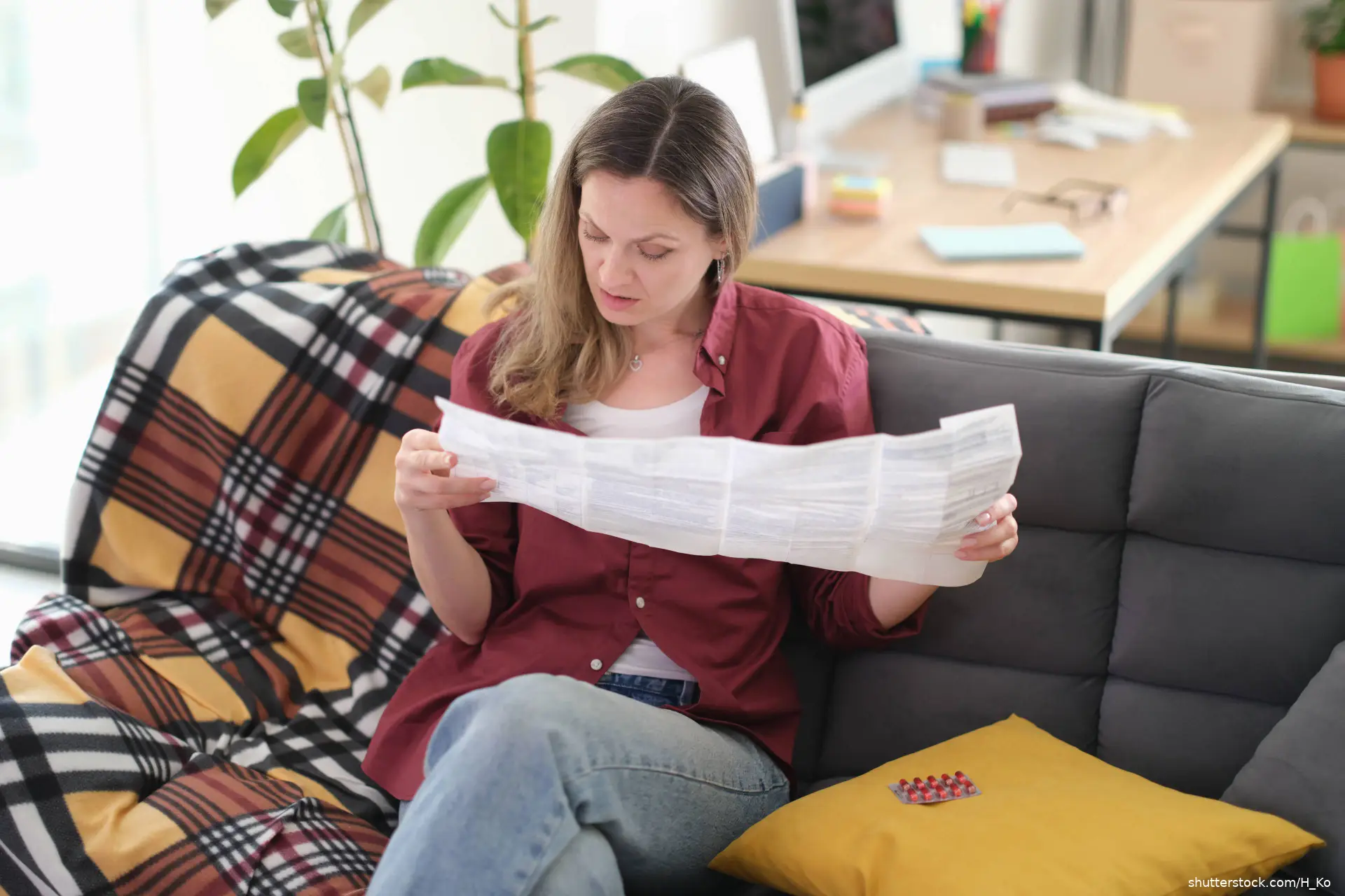 Woman reads medicine leaflet while sitting on sofa