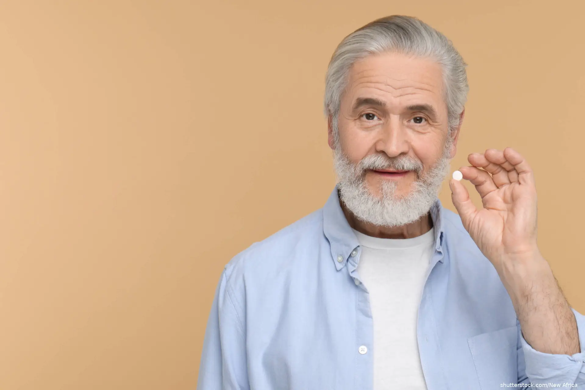 Senior man holding pill on beige background