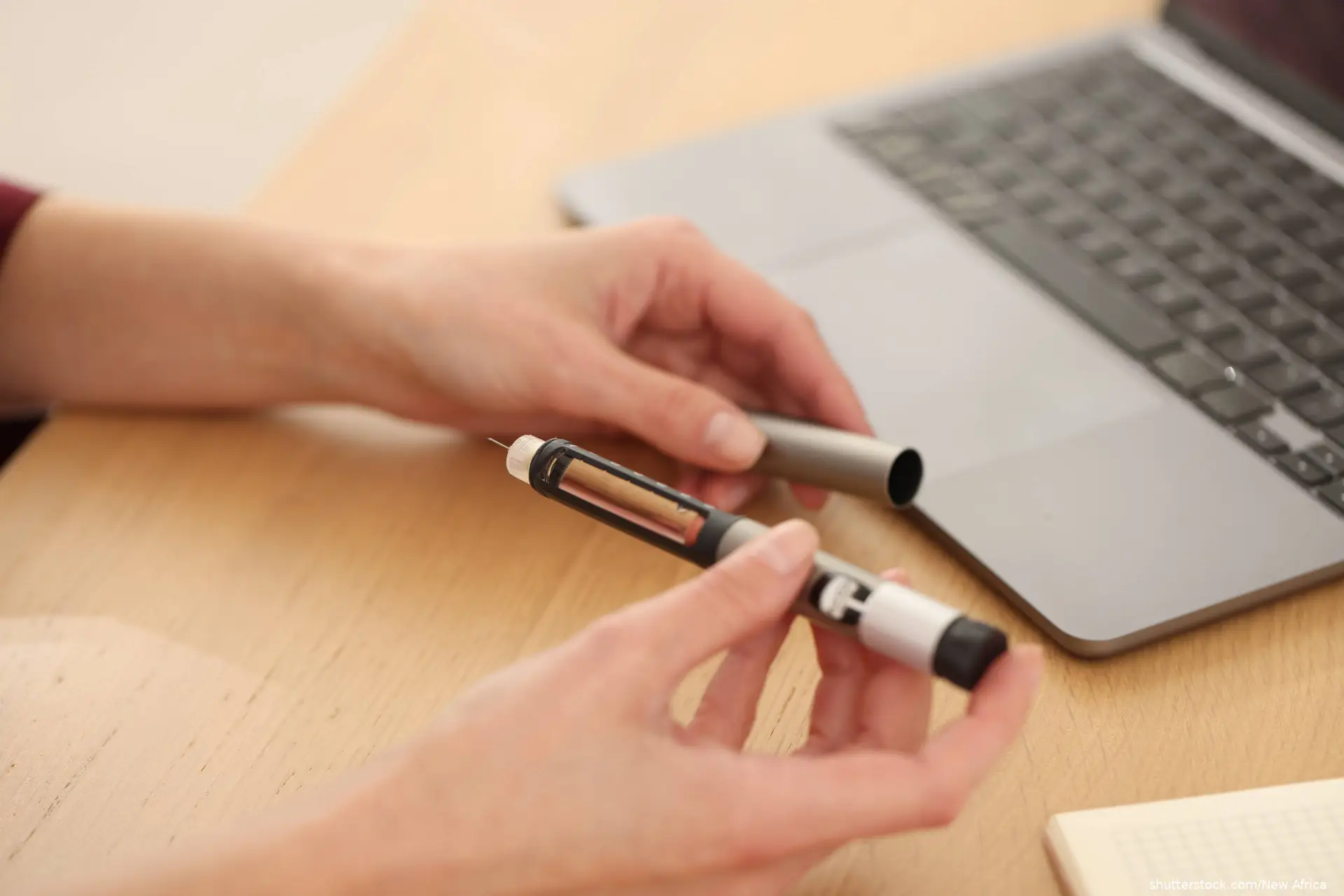 Woman with autoinjector and laptop at wooden table