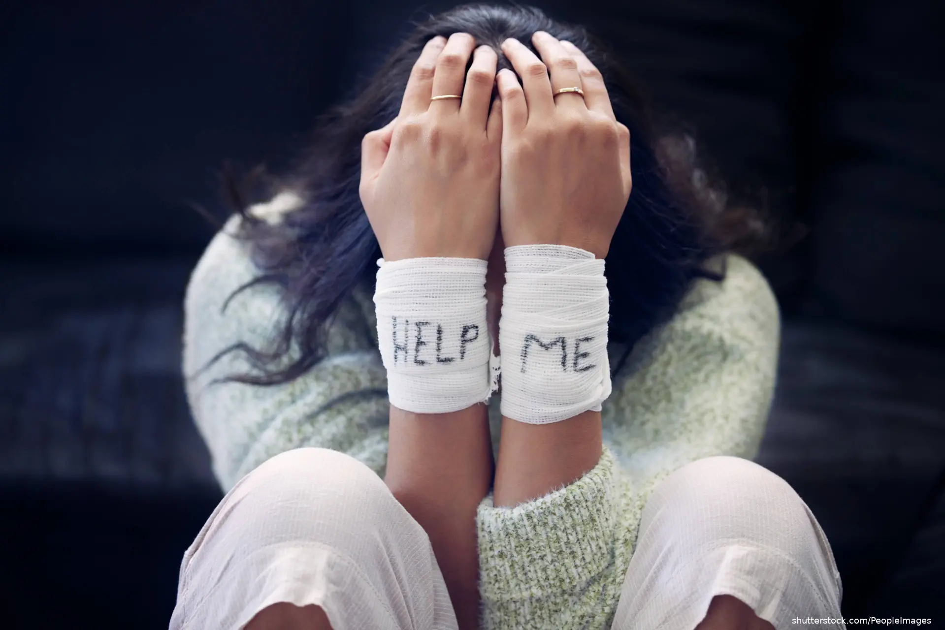 suicidal young girl with bandaged wrists and help me written on bandages