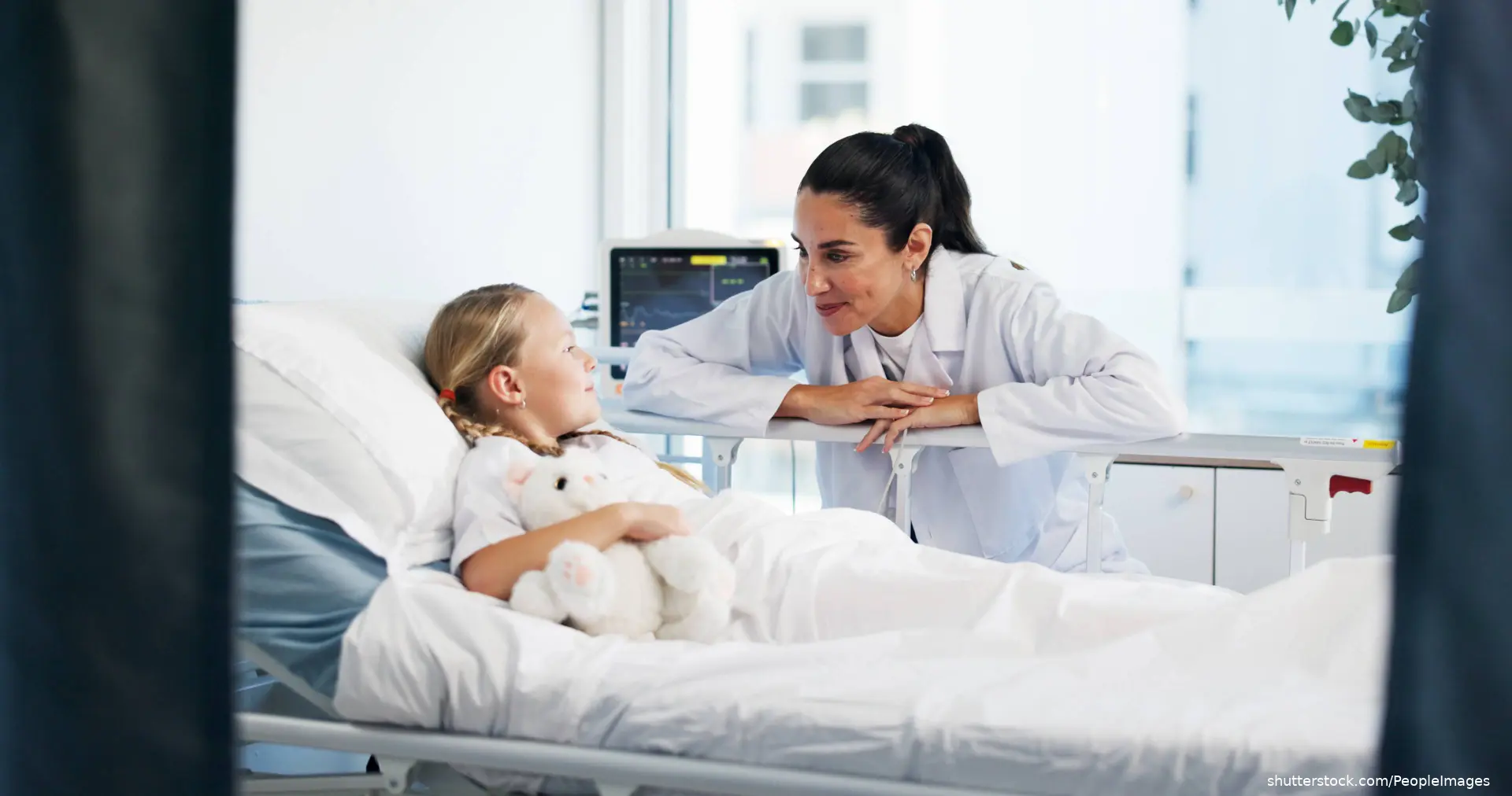 doctor checking on young girl in hospital bed shutterstock_2643868535