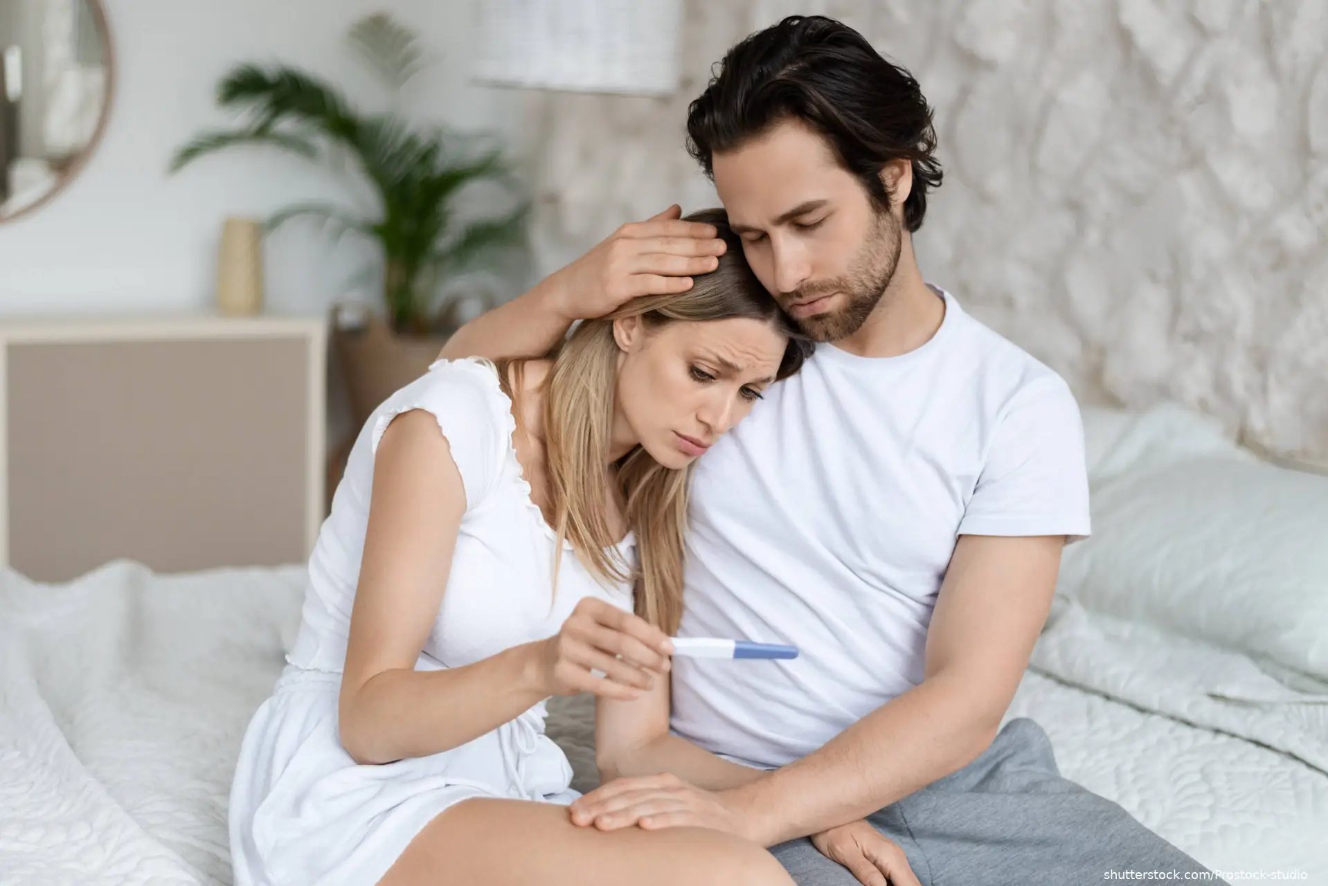 couple sitting on bed with negative pregnancy test