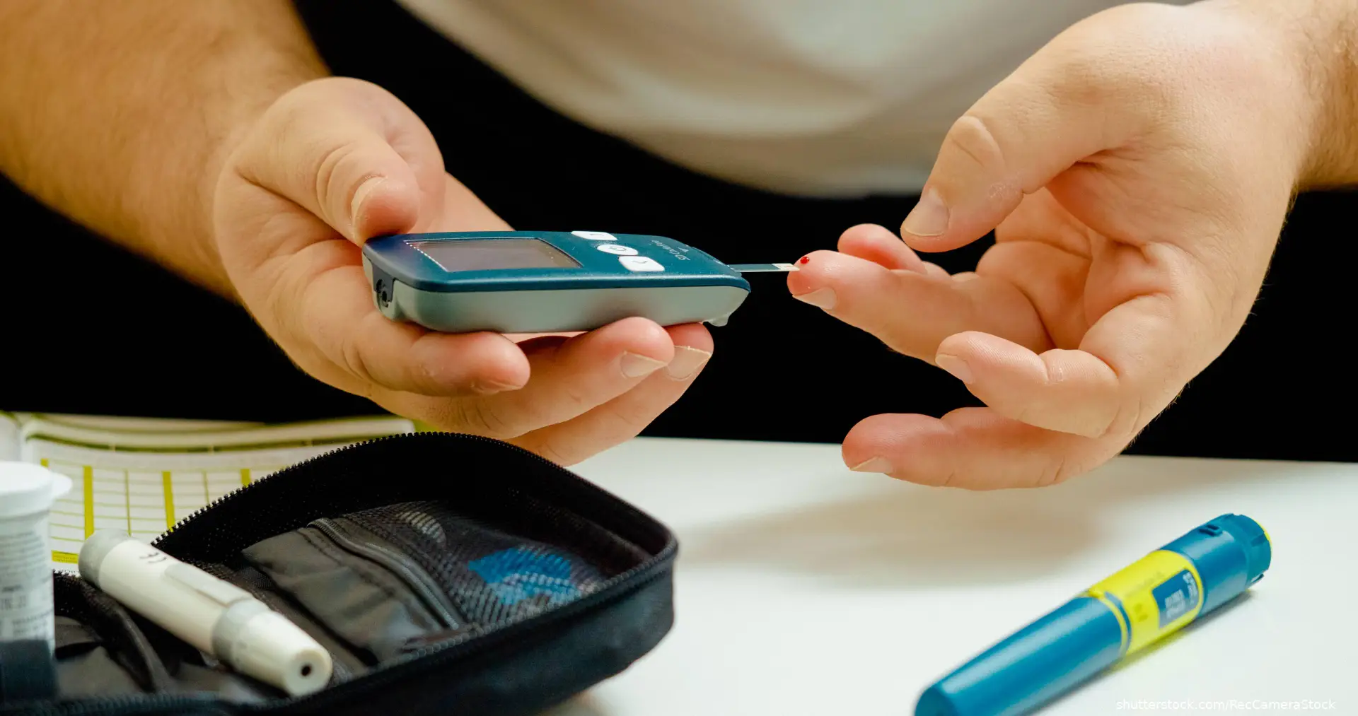image of man testing blood sugar with testing supplies and insulin pen on table