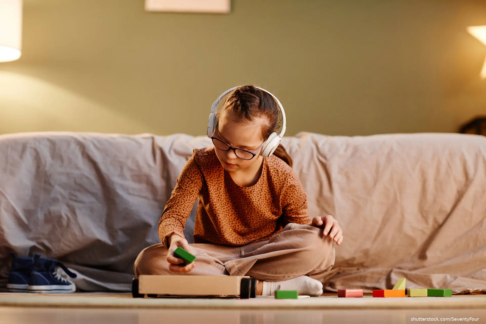 young girl with autism wearing headphones playing with toy blocks alone