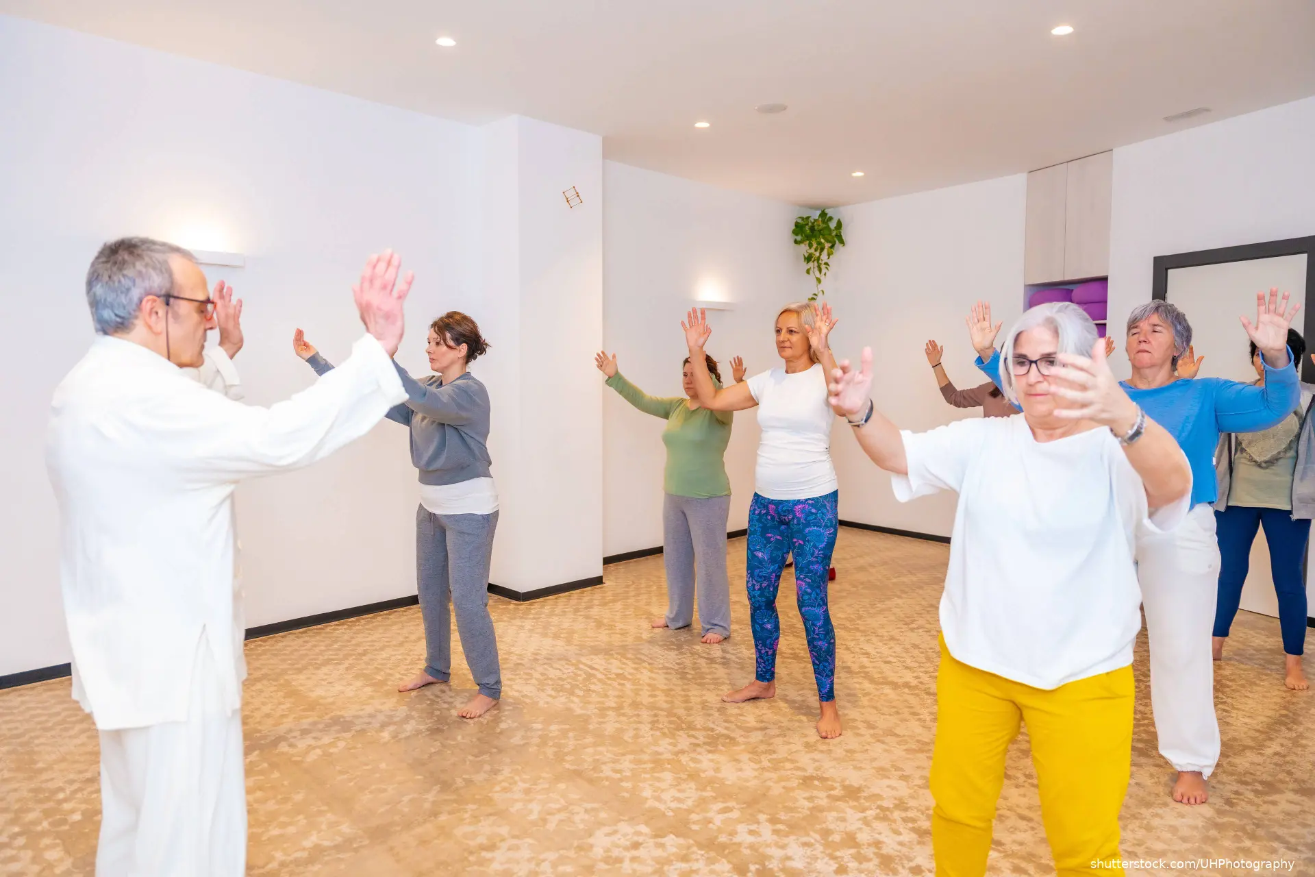 Qi gong male mature teacher leading a class full of mature women in a indoor center