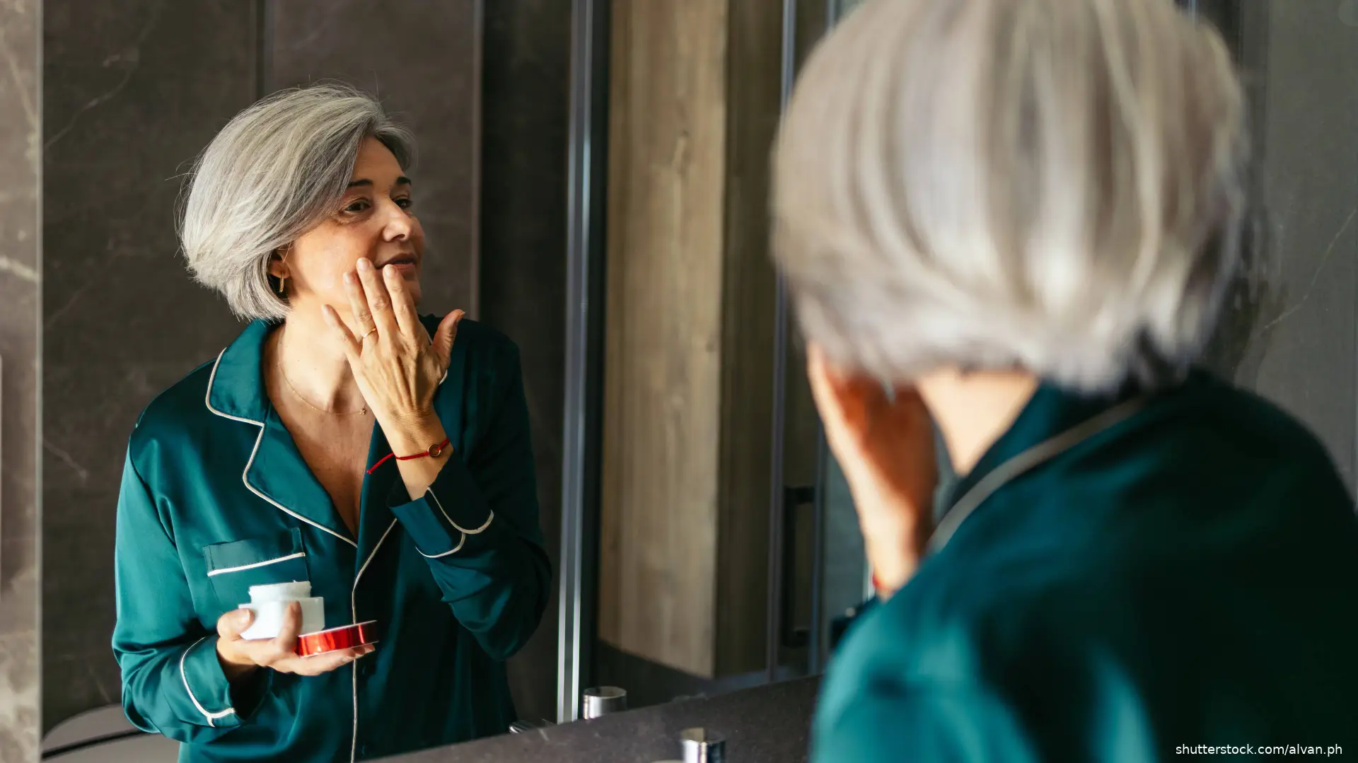 woman applying skincare cream in bathroom mirror