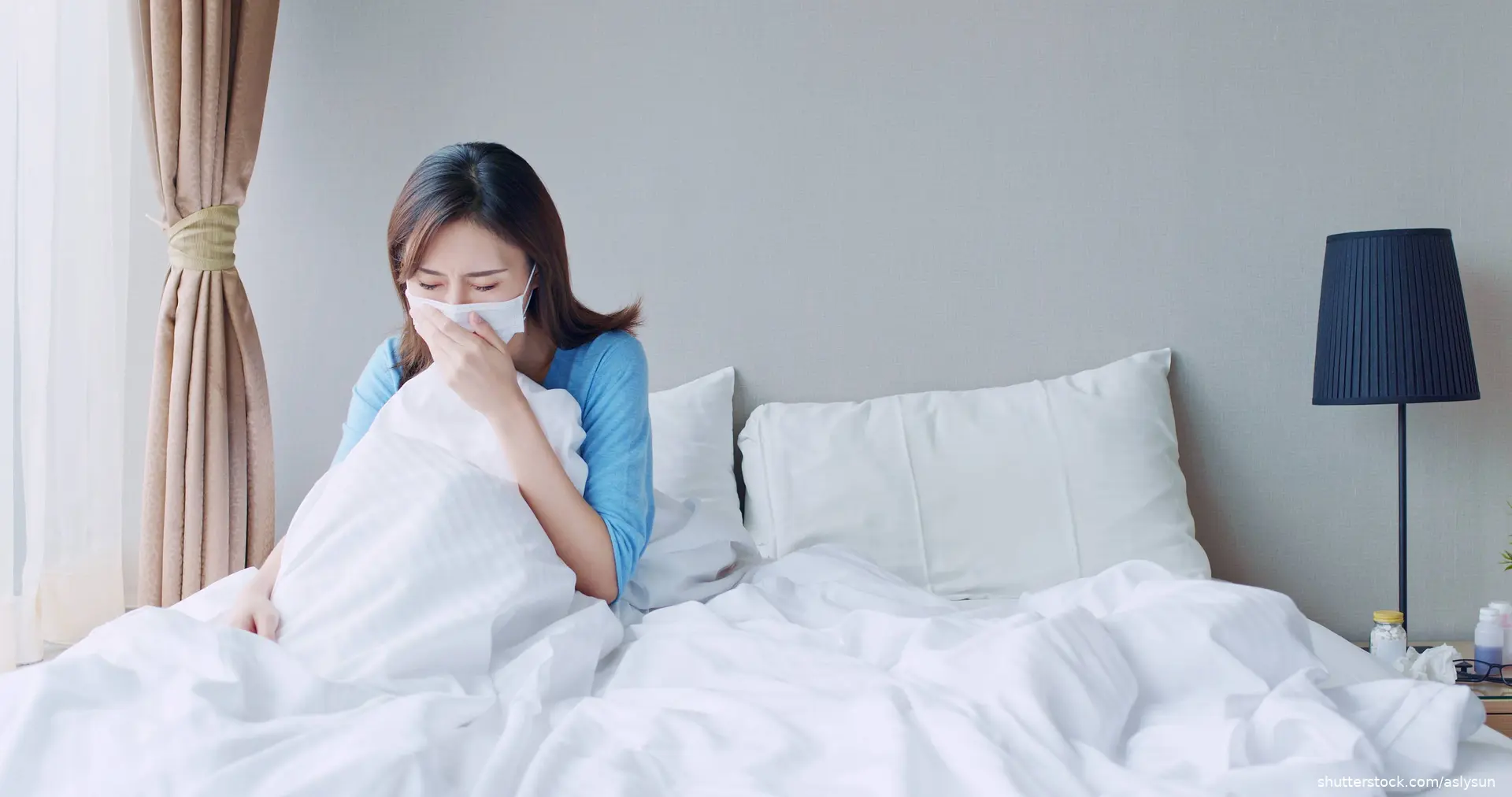 Asian woman in bed with mask on coughing