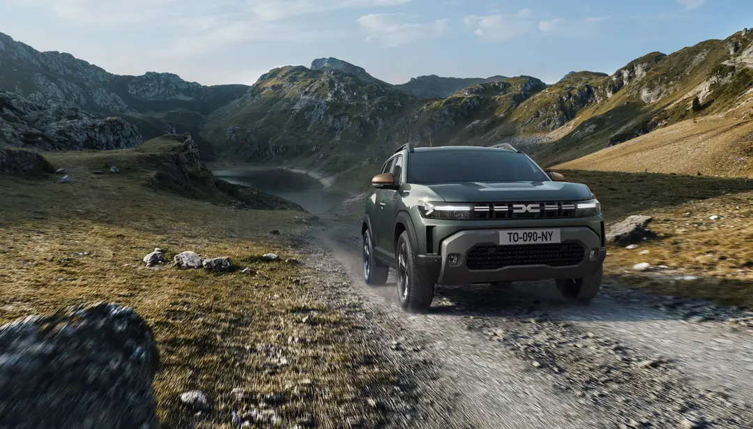 Dacia Duster percorre uno sterrato con sfondo campagne e montagne