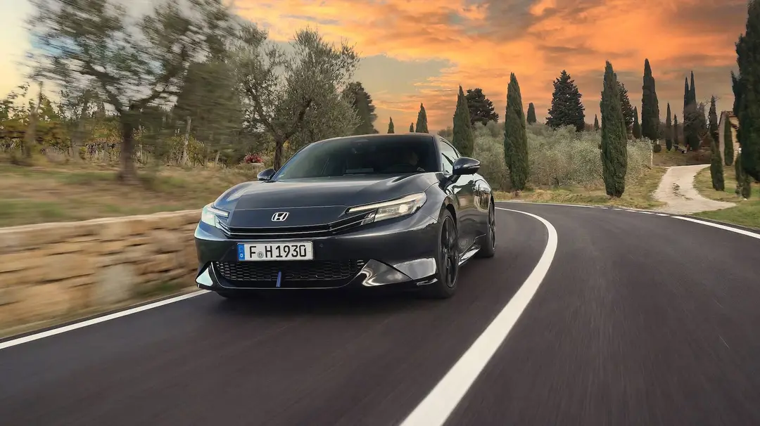 Una foto dinamica dell'anteriore della Honda Prelude Hybrid 2026, verniciata in colore grigio e con un tramonto e delle strade collinari toscane