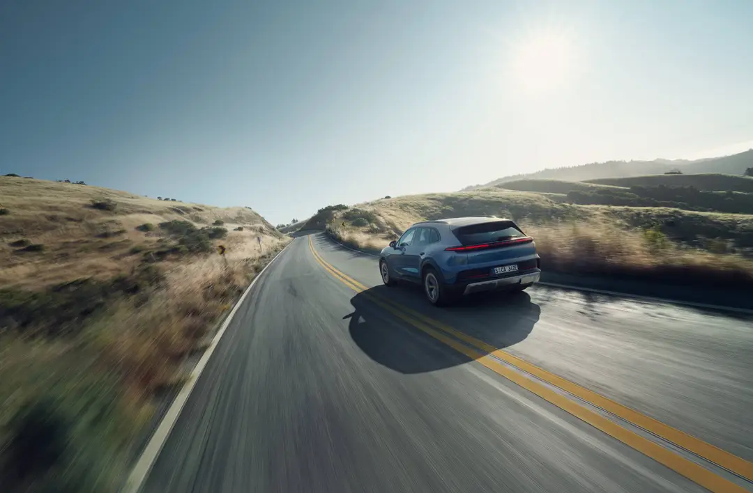 Porsche Cayenne S elettrico dinamica posteriore con sfondo dei prati e la strada