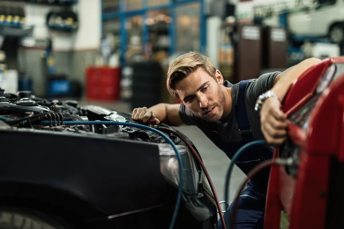 young auto mechanic using compressor while maintaining ac unit car workshop
