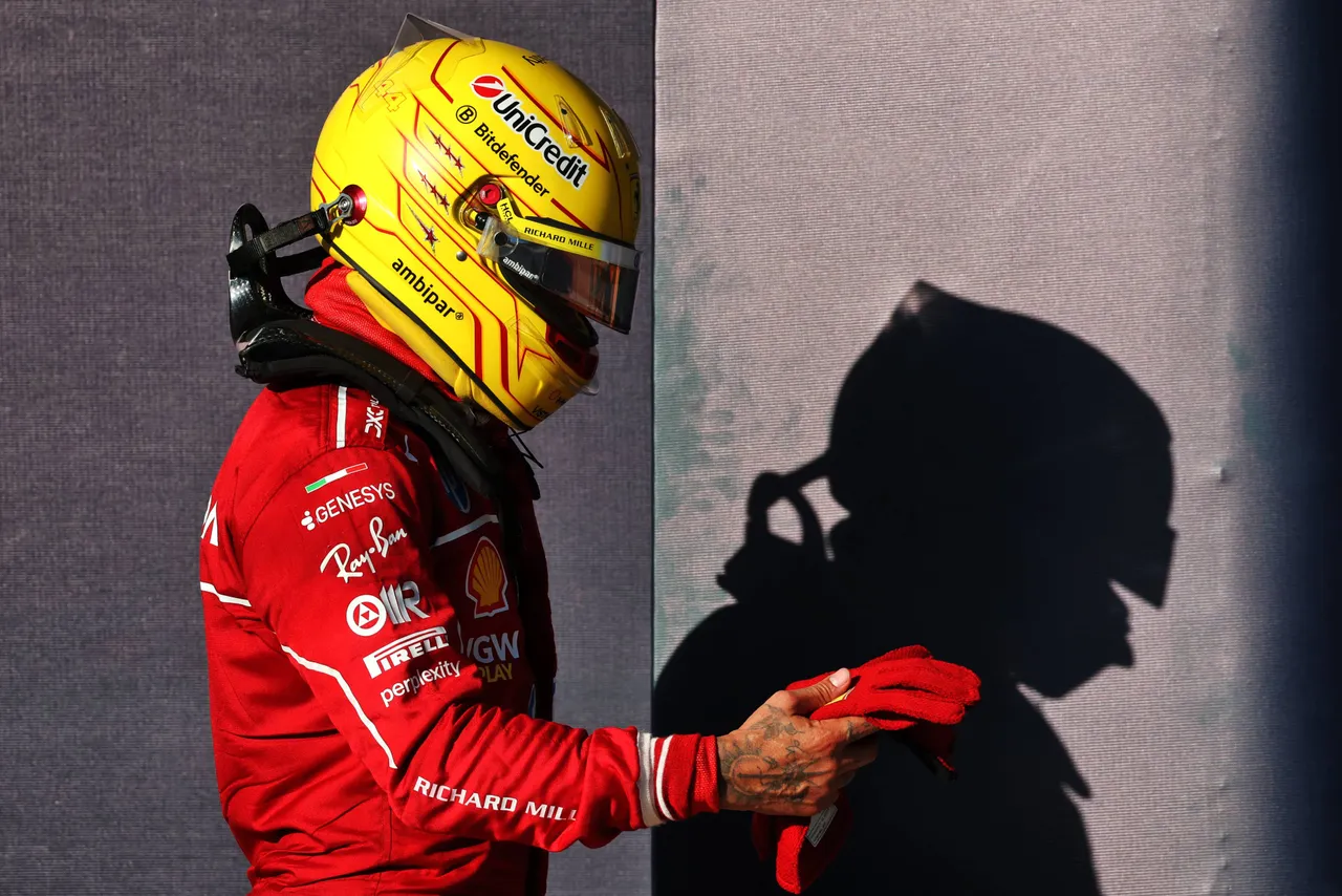 Lewis Hamilton in zijn Ferrari-racepak voor een grijze muur.