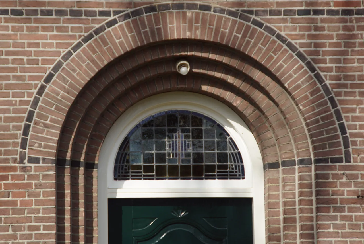 De toepassing van rondbogen, nissen en glas-in-lood met eenvoudige motieven zijn kenmerken van de bouwstijl Amsterdamse School