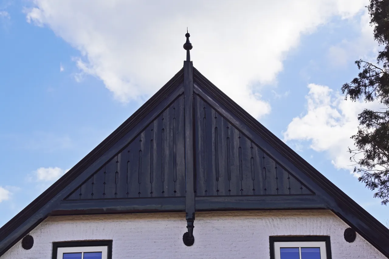 De gevelmakelaar is de verticale middenstijl, welke aan de boven- en onderzijde een versiering heeft. De middenstijl staat tussen de twee windveren en over de horizontale trek[plaat.