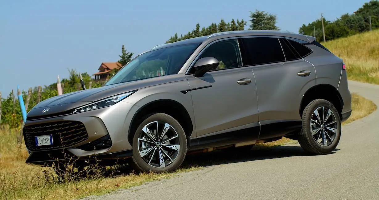 La nuova MG HS hybrid di colore grigio in primo piano con strada e campi sullo sfondo