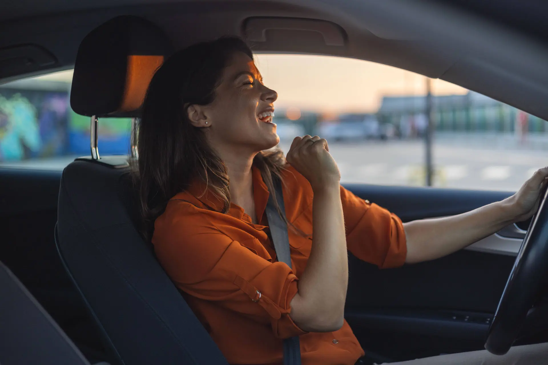 Donna che canta dietro al volante di una vettura vestita di arancione