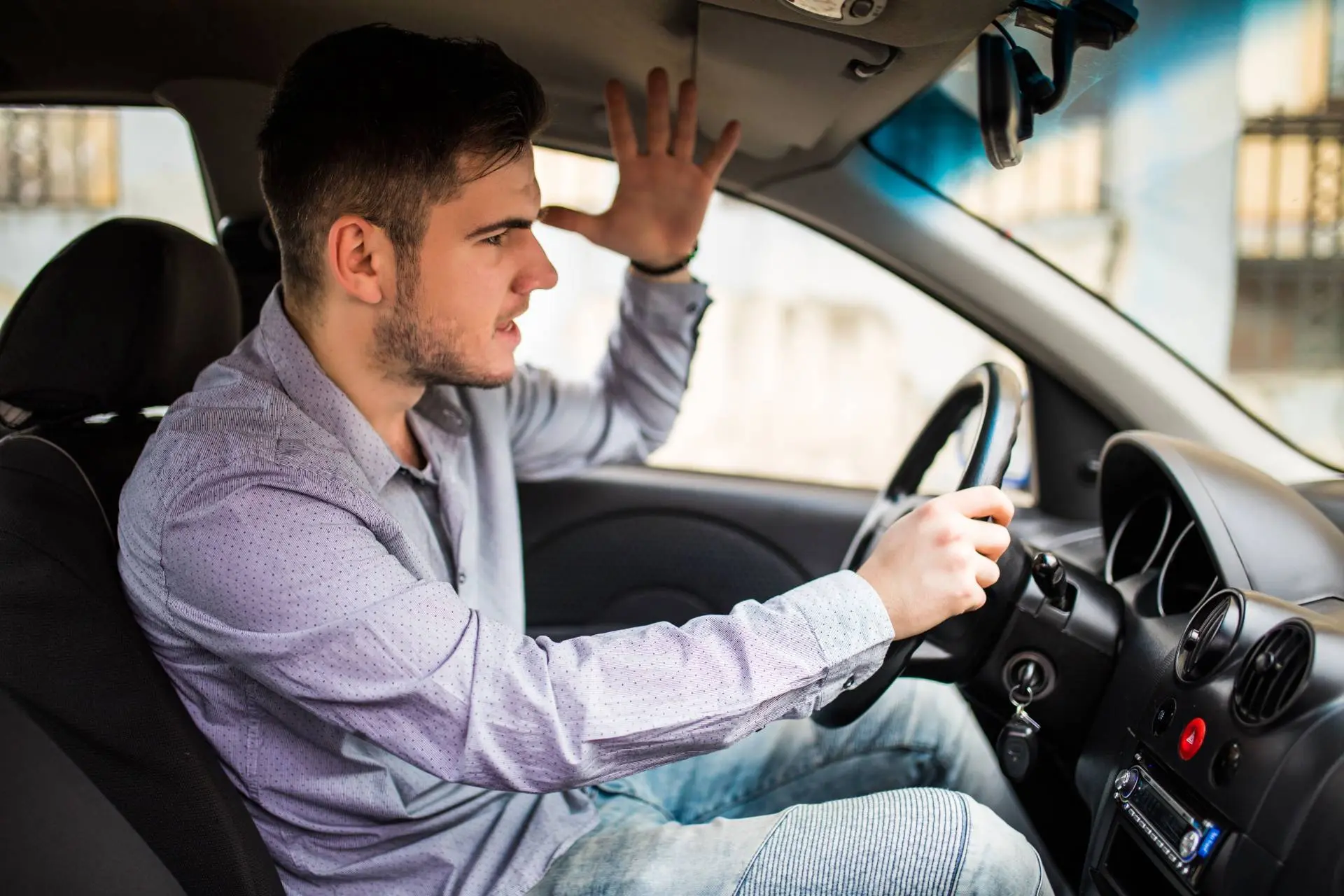 Abitudini quotidiane al volante che costano di più agli italiani- Ragazzo arrabbiato al volante che alza il braccio e ha espressione innervosita