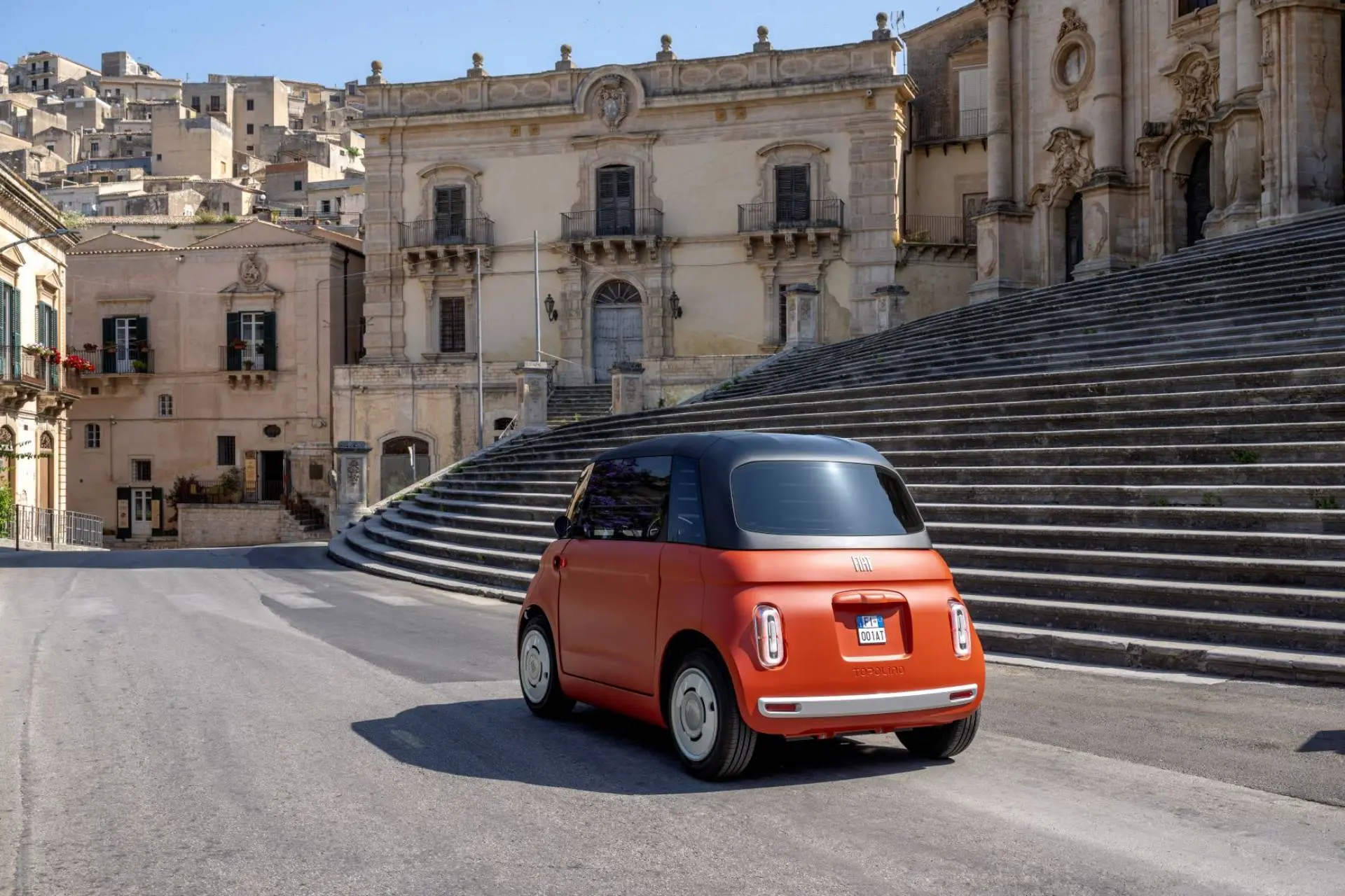 FIAT Topolino Corallo che percorre una strada davanti a una scalinata e un palazzo d'epoca