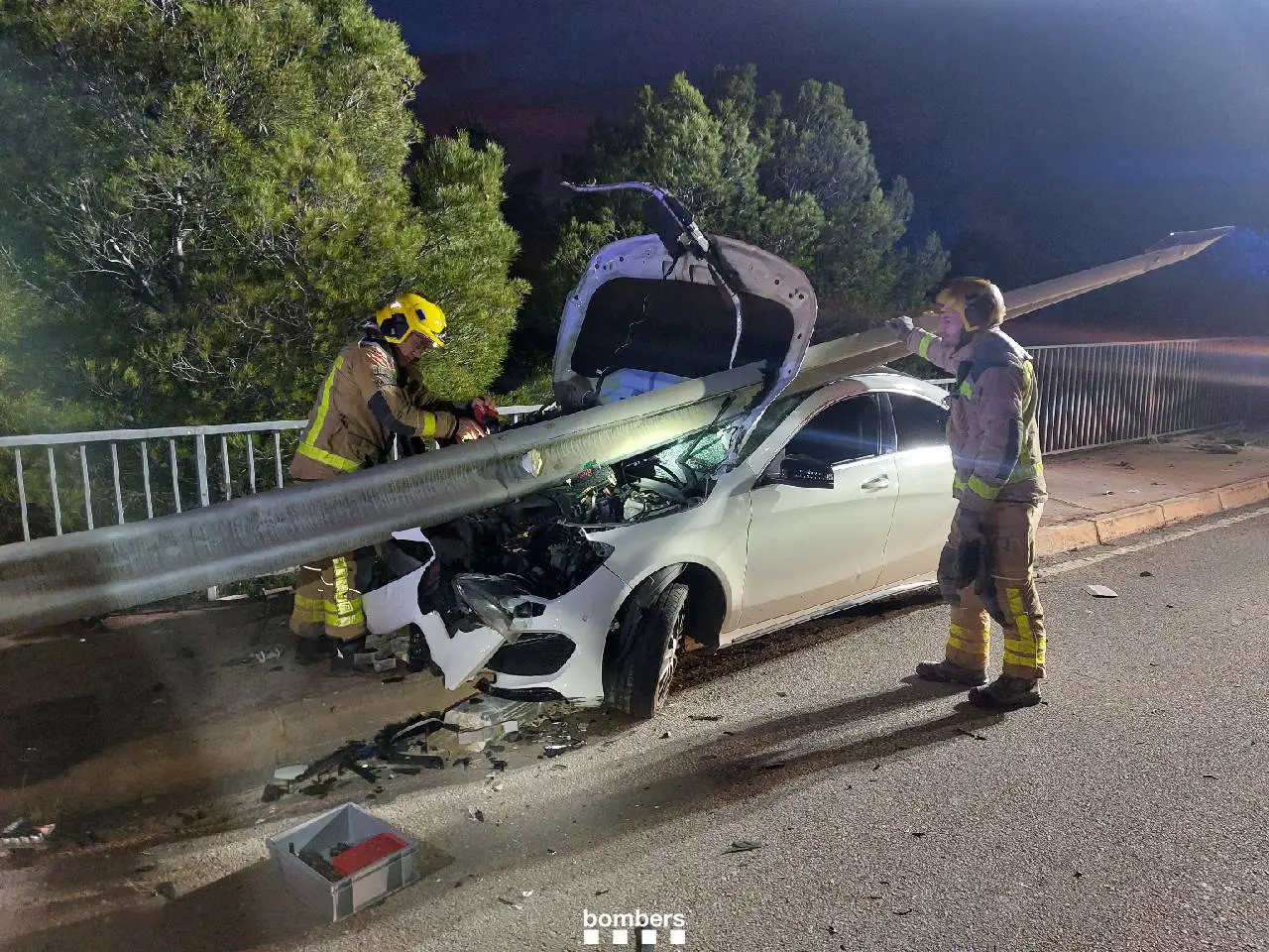 Nell'immagine si può vedere come una macchina incidentata abbia divelto il guardrail e abbia sfondato il cofano senza intaccare il parabrezza. Vicini alla vettura si vedono due vigili del fuoco che lavorano per sistemare la situazione