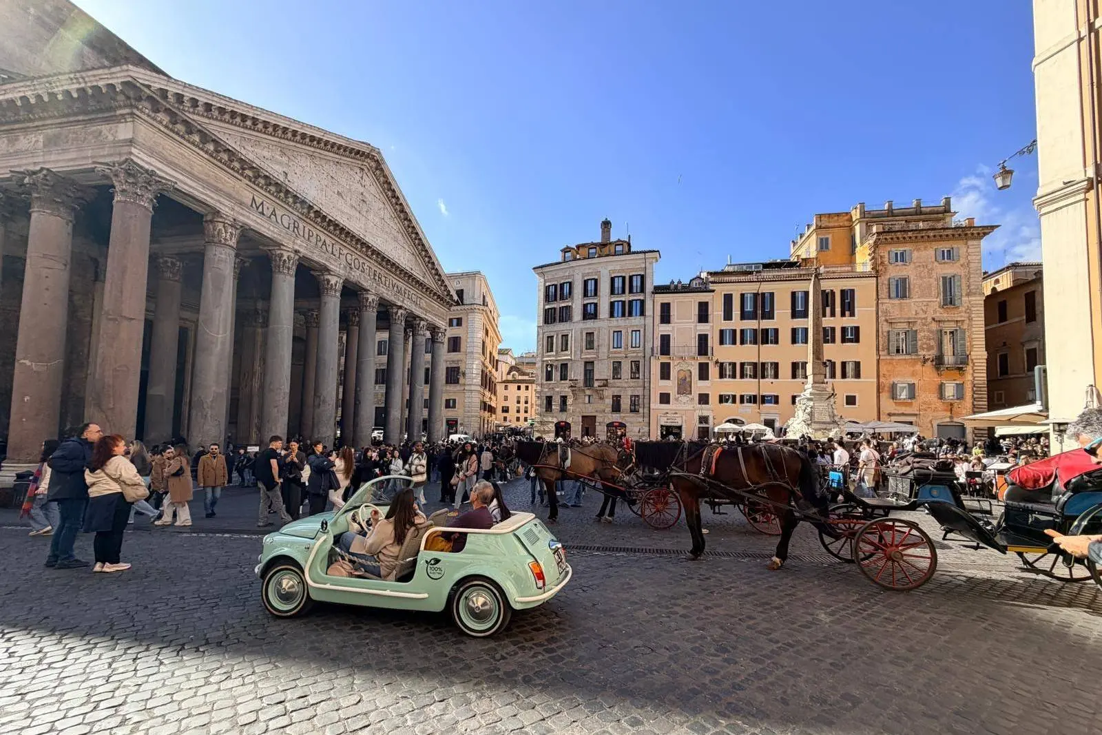 Immagine che ritrae i turisti che affollano la zona del pantheon di roma sotto il sole e con ua 500 d'epoca in primo piano