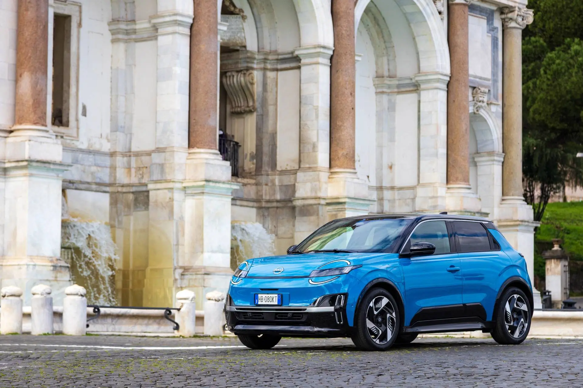 Nuova Nissan MICRA di colore azzurro laterale frontale con sfondo di un palazzo storico di roma
