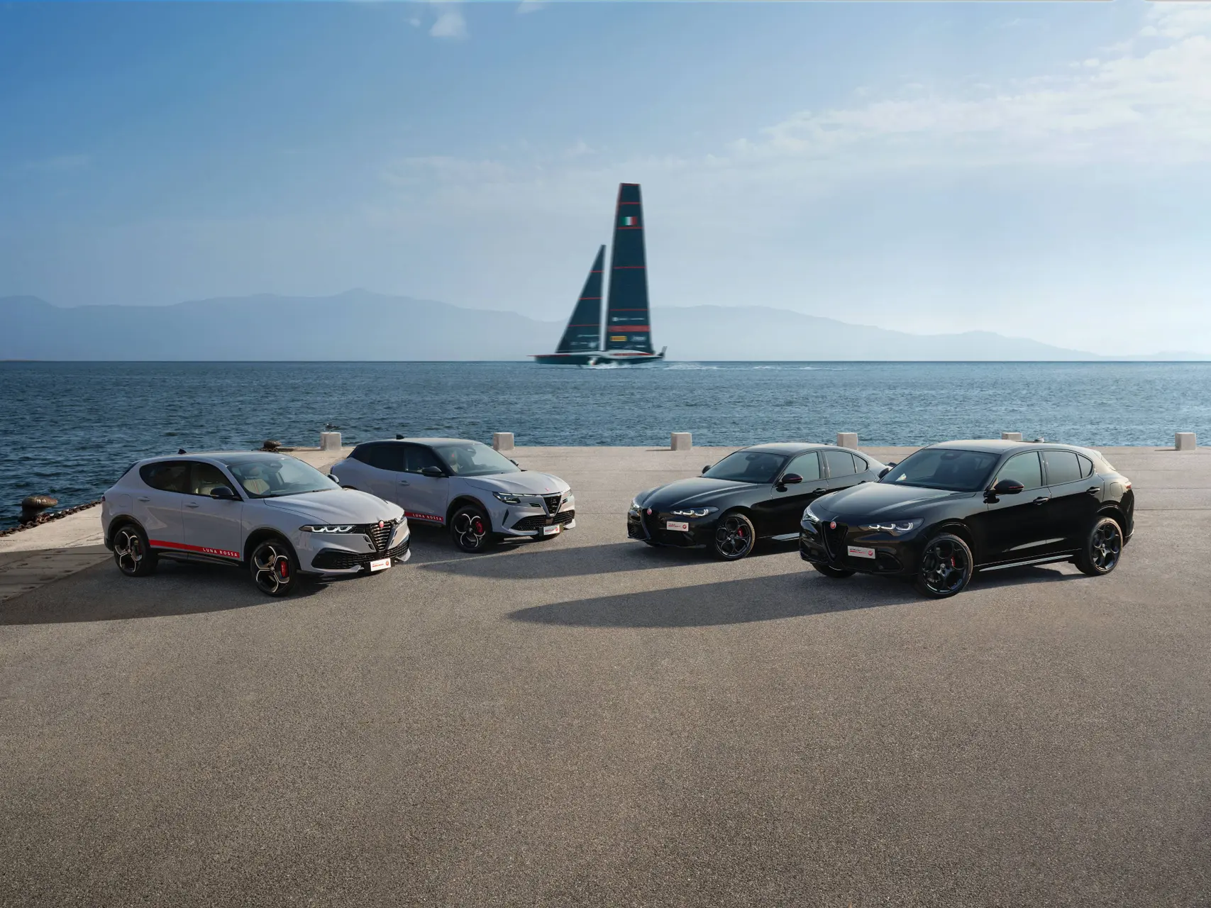 Nell'immagine si vede la gamma di Alfa Romeo in collaborazione con Luna Rossa. Sullo sfondo si vede una delle vele da gara di Luna Rossa