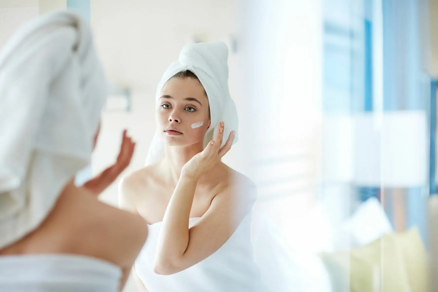 Young,Woman,Applying,Foundation,Or,Moisturizer,On,Her,Face,In