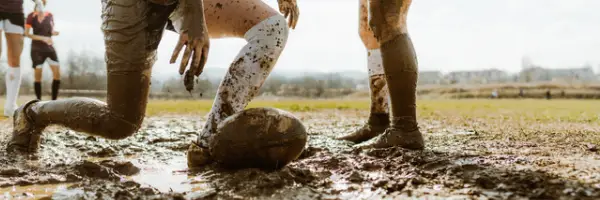 Rugby pitch with 3 players and ball, pitch deep in mud