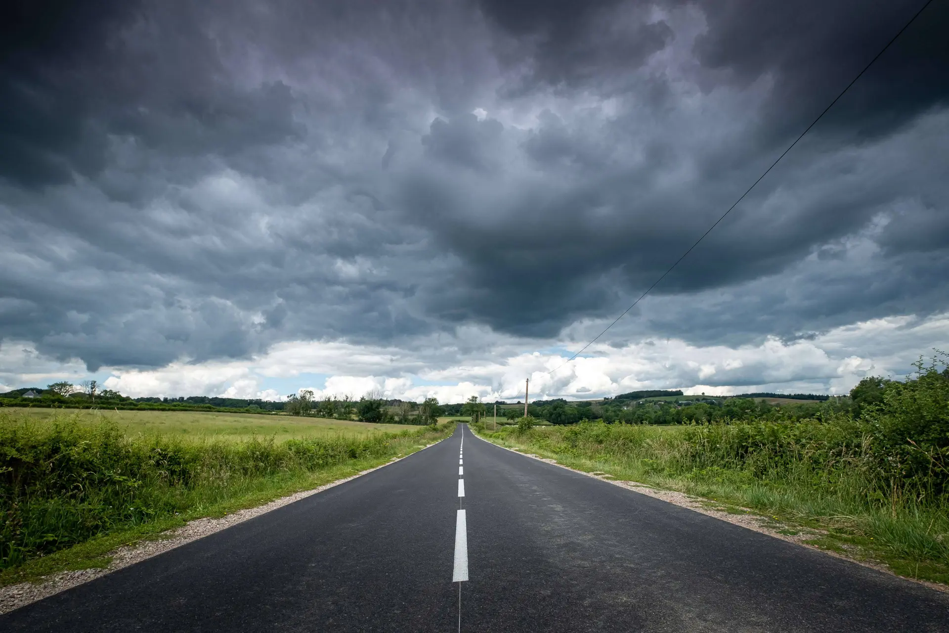 beautiful-view-empty-road-surrounded-by-greenery-dark-storm-clouds