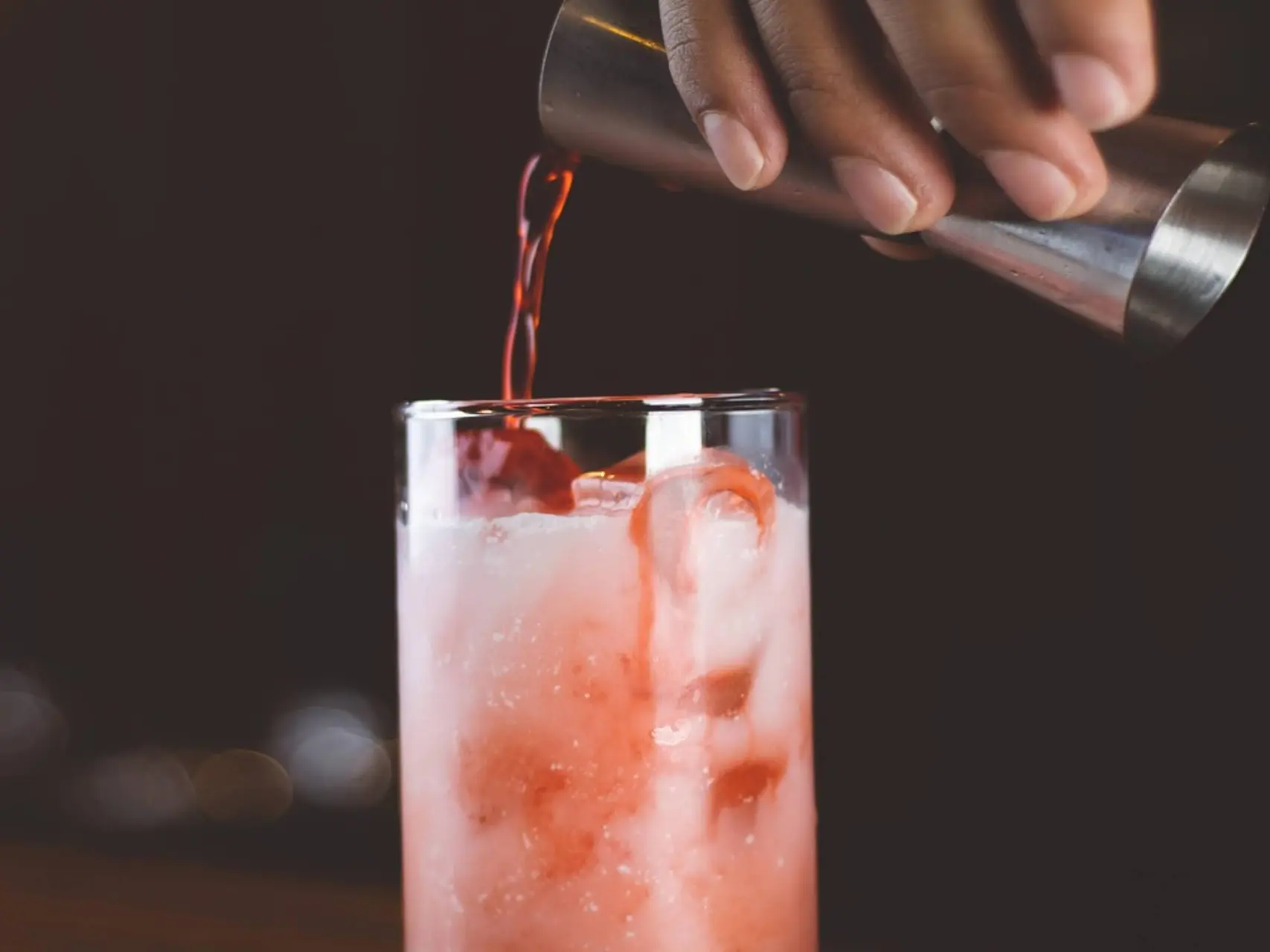 een glas met een cocktail waarin net een nieuw ingredient geschonken wordt.