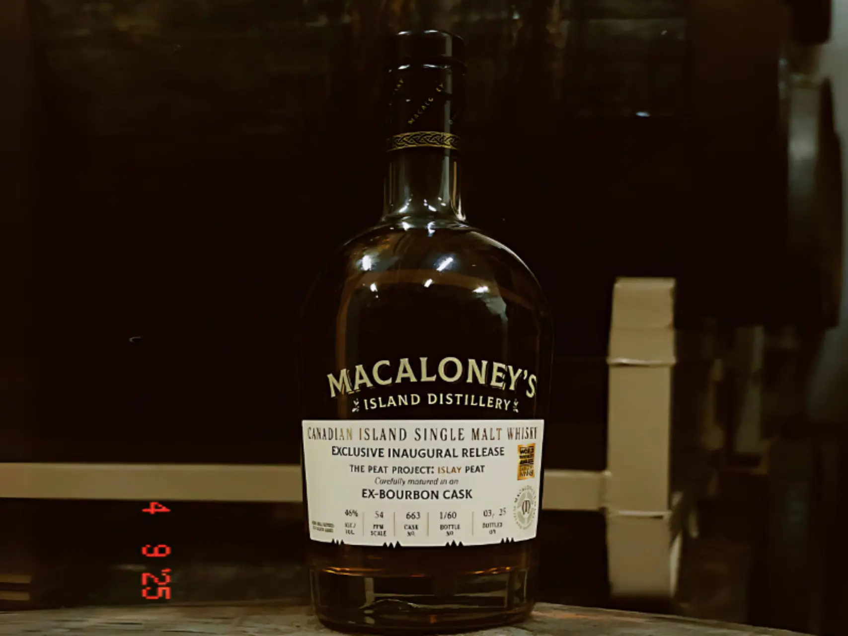 Een fles Macaloneys Island The Peat Project Islay Peat op een vat