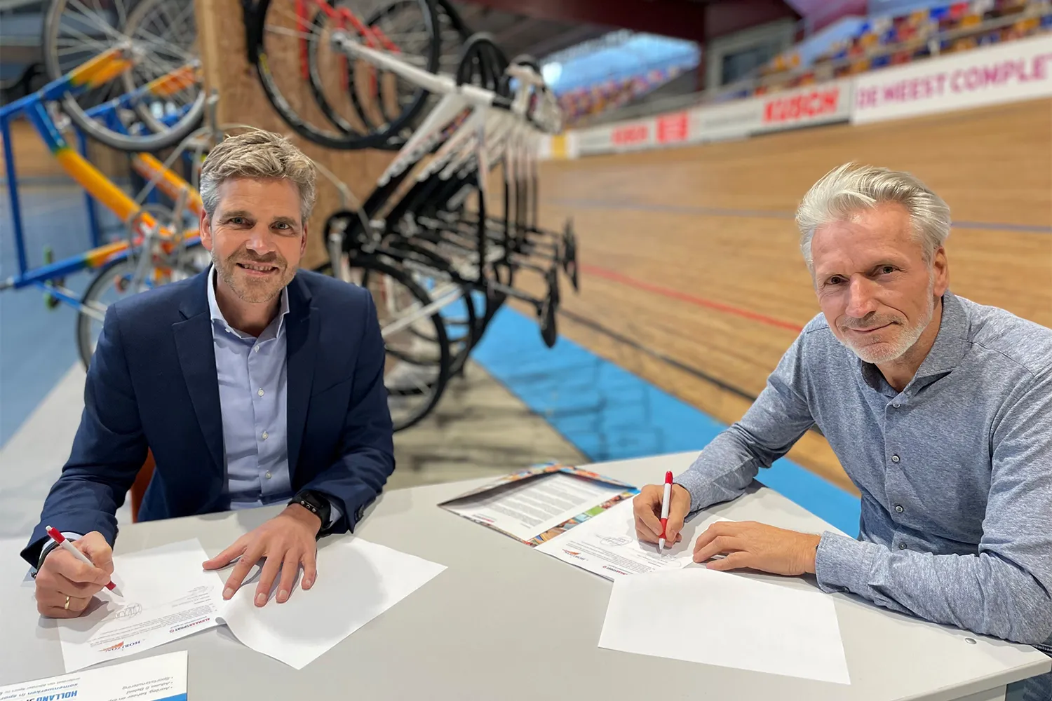 arjan kloppers en vincent thijssen tekenen de overeenkomst bij de alkmaarse wielerbaan