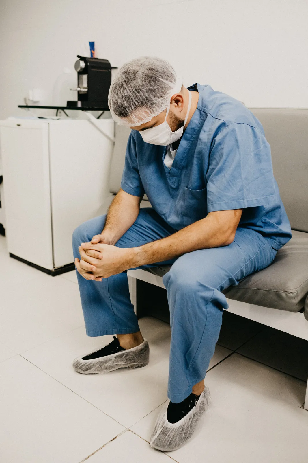 canva man wearing blue scrub suit and mask sitting on bench