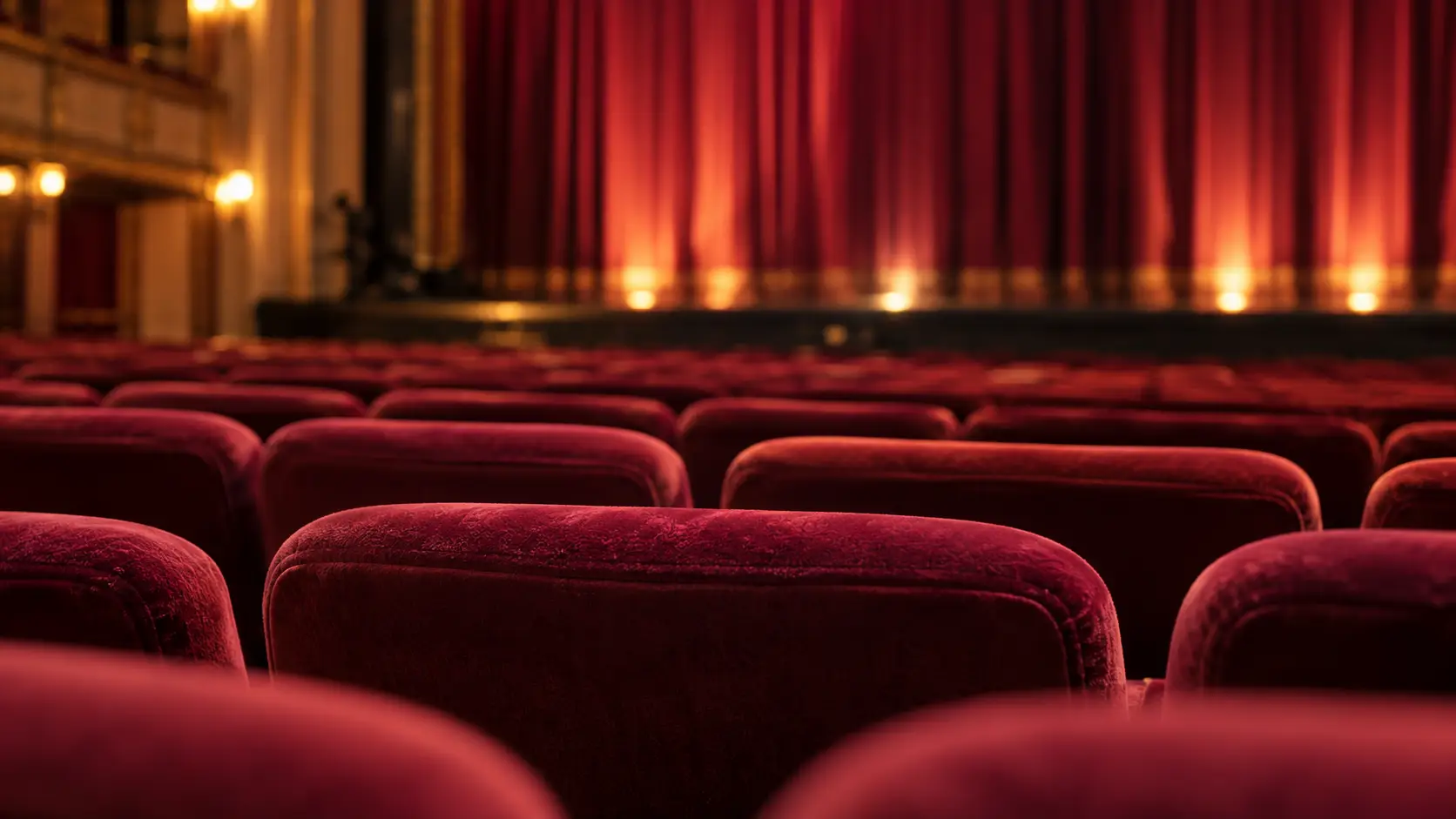 Rode theaterstoelen met een verlicht podium en gesloten gordijn op de achtergrond