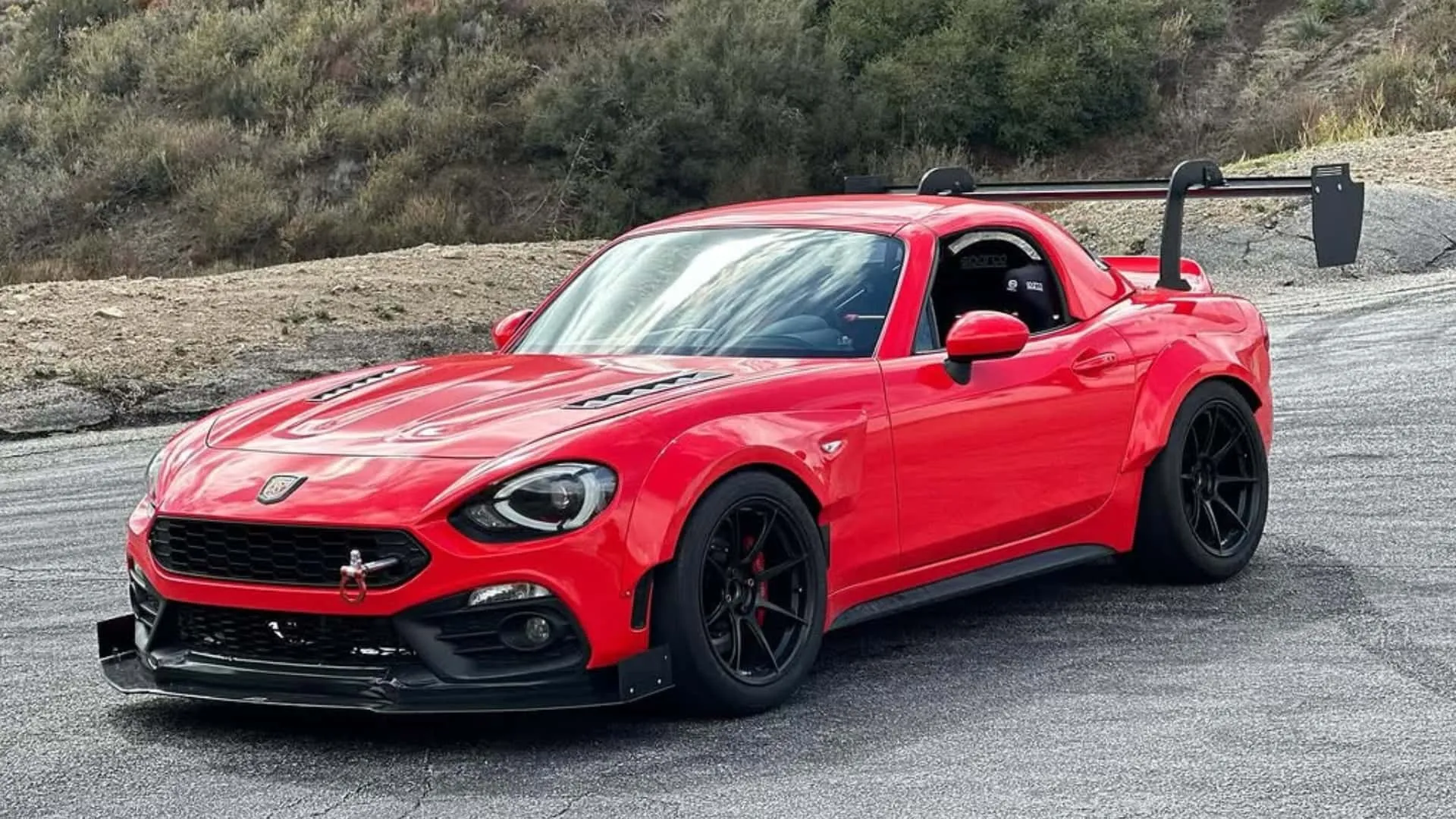 nell'immagine si vede una 124 spider rossa di fiat con un kit widebody. La foto è stata scattata su una strada collinare