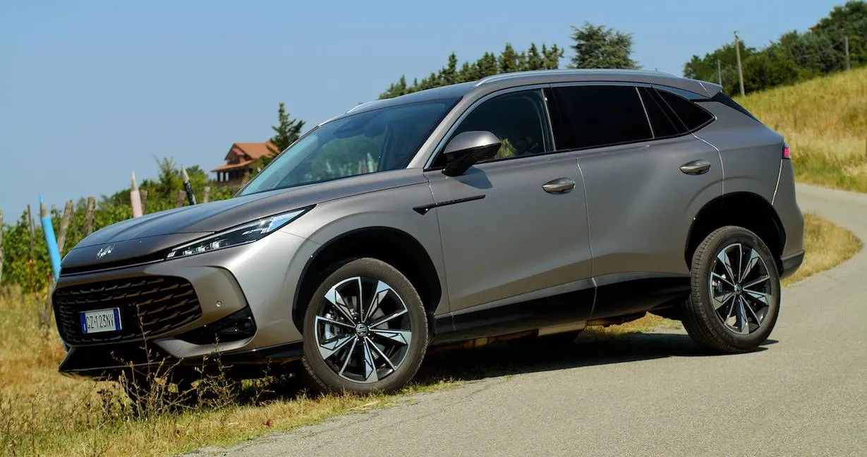 La nuova MG HS hybrid di colore grigio in primo piano con strada e campi sullo sfondo