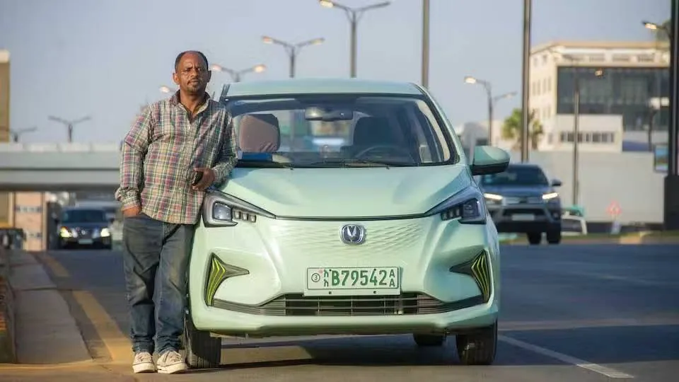 Nell'immagine si vede un veicolo elettrico in Etiopia e il guidatore appoggiato fuori sul lato destro della macchina. Sullo sfondo si nota un cavalcavia e dei lampioni