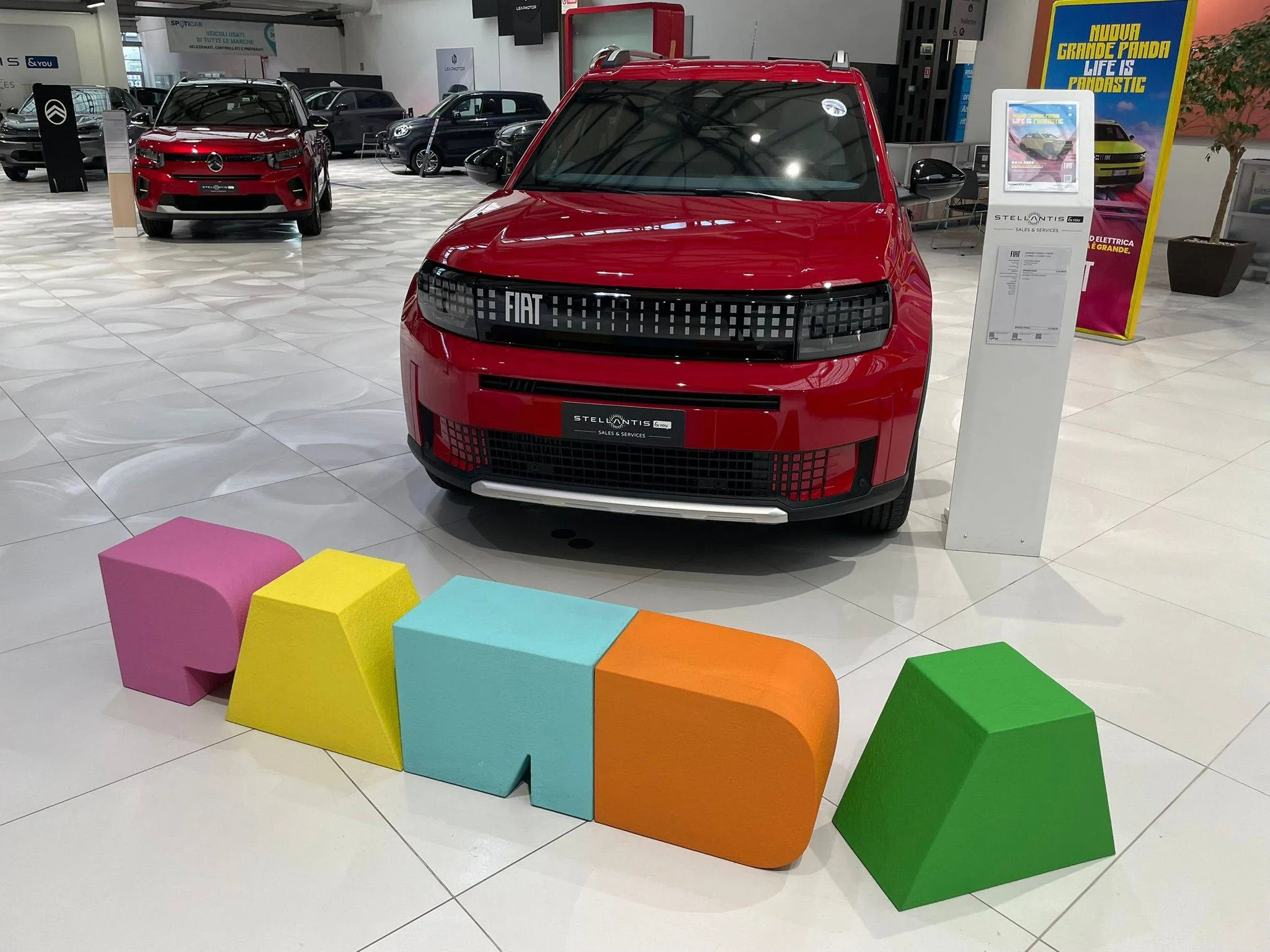 FIAT Grande Panda rossa in salone con scritta panda colorata su sfondo pavimento bianco
