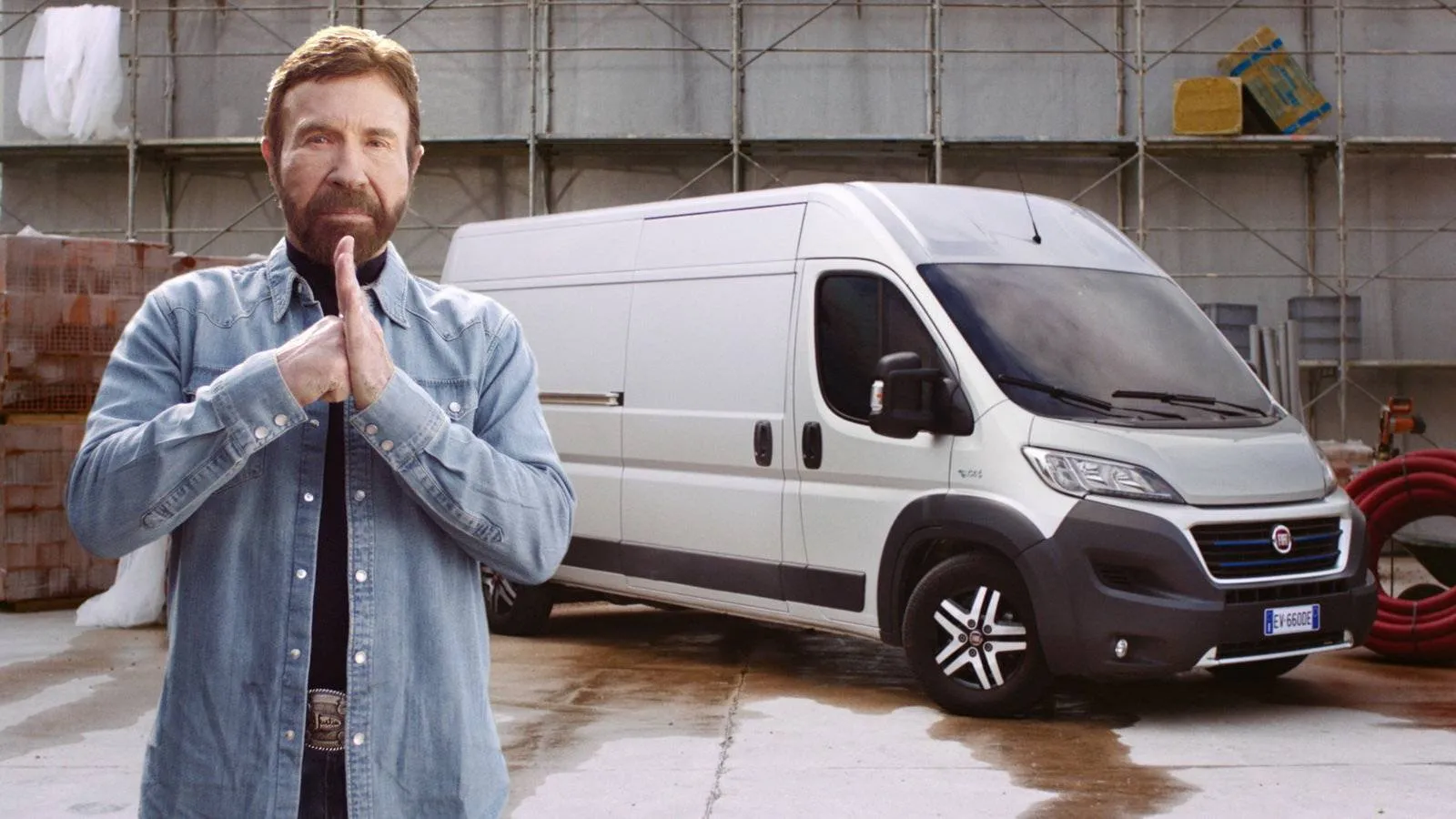 chuck norris affianco a un fiat professional ducato. l'attore batte il pugno contro la mano aperta e sullo sfondi il ducato grigio e un cantiere