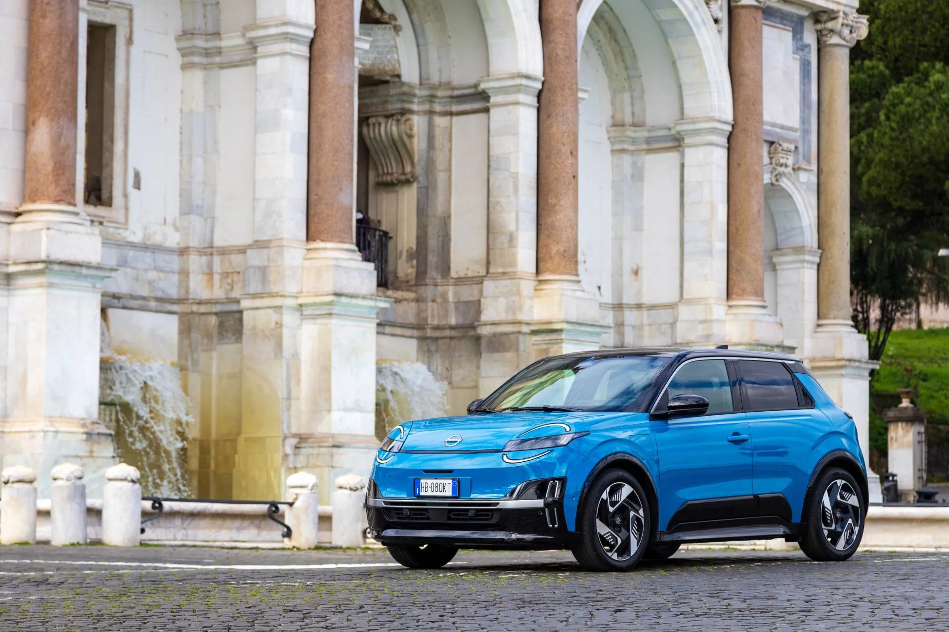 Nuova Nissan MICRA di colore azzurro laterale frontale con sfondo di un palazzo storico di roma