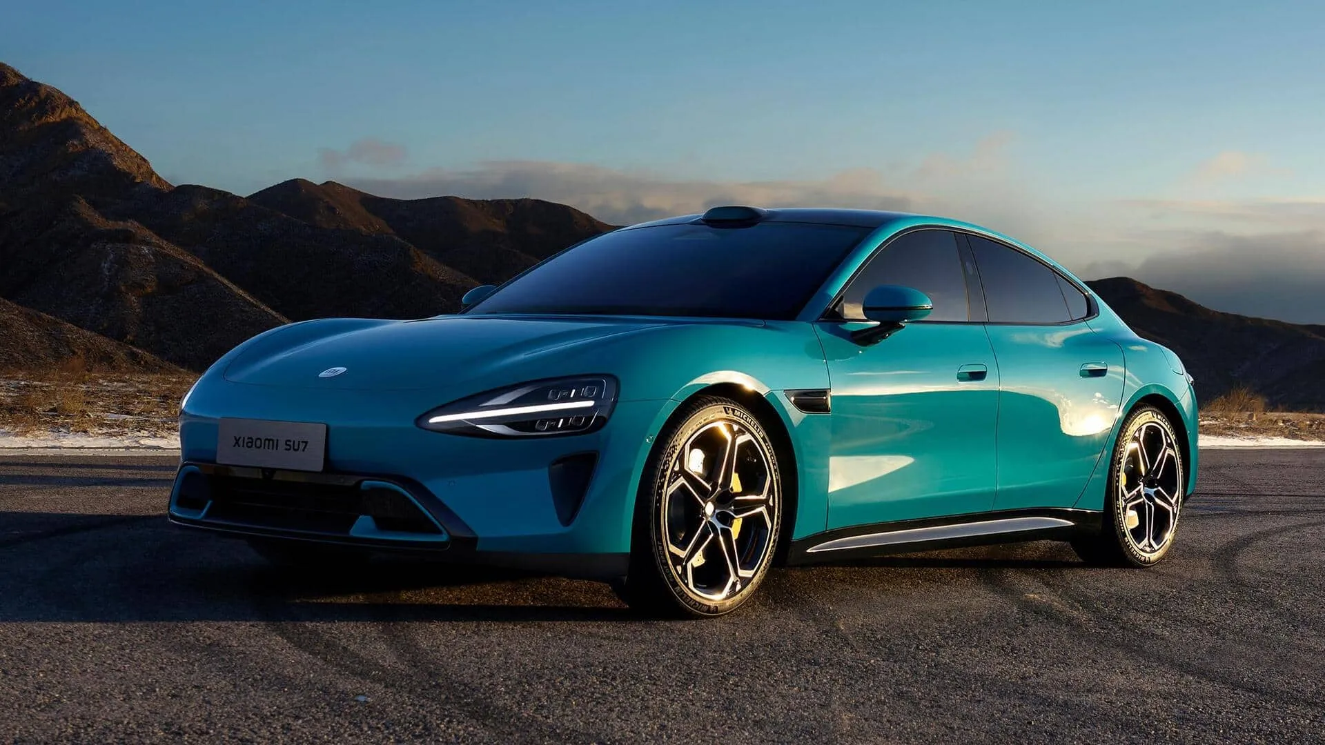 Nell'immagine si vede la Xiaomi SU7 blu in strada su uno sfondo di montagna