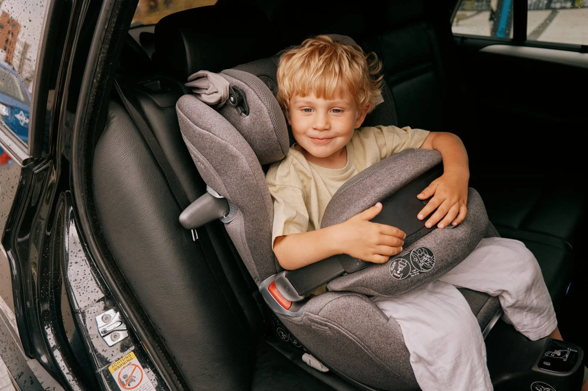 bambino biondo seduto su un seggiolino auto ripreso lateralmente frontale